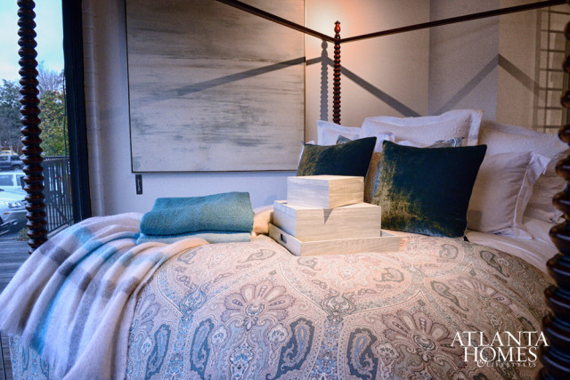 Bedroom with a four-poster bed, paisley comforter, teal velvet pillows, stacked decorative boxes, and a large abstract painting on the wall.