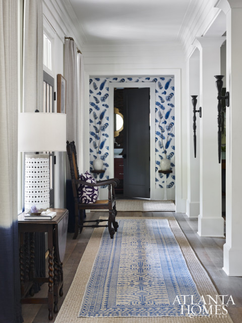 Hallway with white walls, blue feather wallpaper, a wooden chair with a patterned cushion, and a long runner rug with blue geometric patterns over a natural fiber rug.