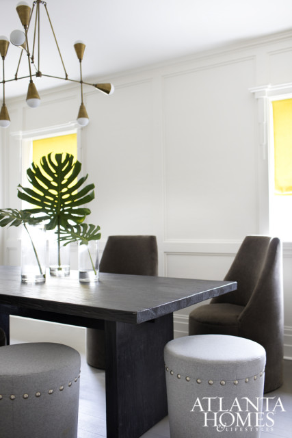 Dark wood dining table with monstera leaves in glass vases, upholstered stools, and modern brass chandelier.