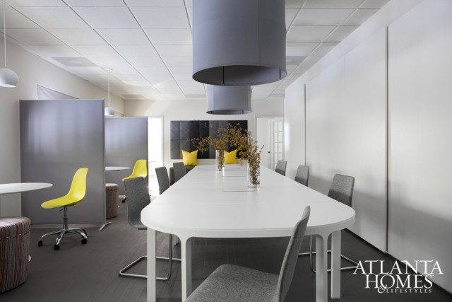 Modern conference room with a long white table, gray upholstered chairs, yellow accent pillows, and large gray pendant lights overhead.
