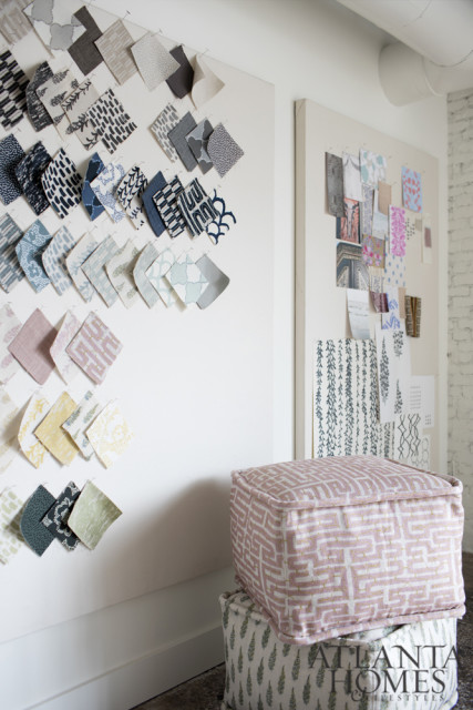 Fabric swatches pinned to white boards on a wall, with two patterned poufs in the foreground.