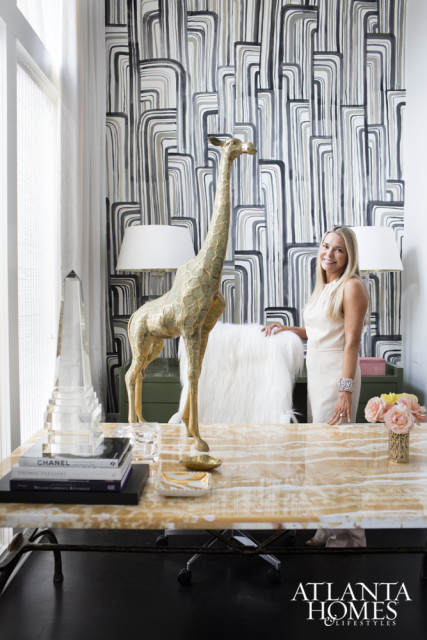 Woman standing behind a desk with a marble top, a gold giraffe statue, and abstract wallpaper.