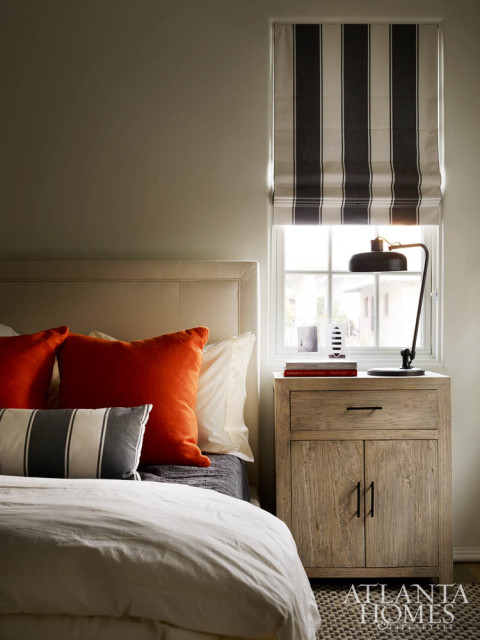 Deep orange pillows pop against this bedroom’s otherwise neutral palette.