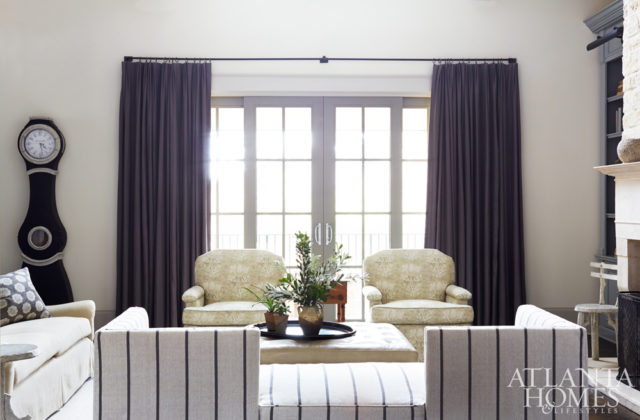 A linen-striped Jacquard fabric from Kravet covers the angled couch in the family room, while charcoal Pindler drapes anchorthe room’s warm gray color scheme.