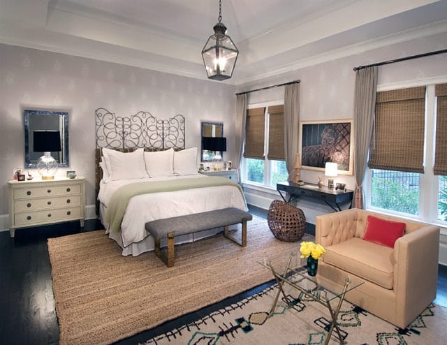Guest bedroom with a tufted cream armchair, glass coffee table, jute rug, and a metal-frame bed with white linens and a pale green throw.