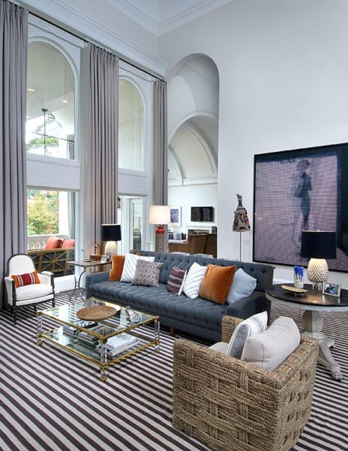 Gray tufted sofa with assorted throw pillows on a striped rug in a living room with high arched windows and vaulted ceilings.