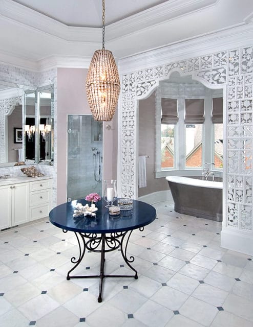Master bathroom with marble tile floor, white cabinetry, freestanding tub, glass shower, and a dark blue round table with a crystal chandelier above.