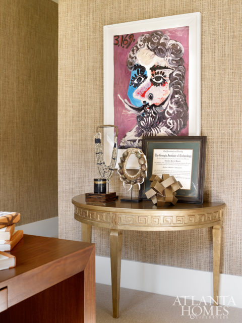 A prized lithograph by Pablo Picasso is displayed among other objets d’art on a Mr. Brown demuline. A grasscloth wallcovering by Phillip Jeffries delivers polished ambience in the study.