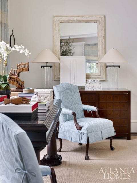 Light blue upholstered armchair with ornate wooden legs and a matching chair in the foreground, placed in front of a dark wood dresser and a large ornate mirror.