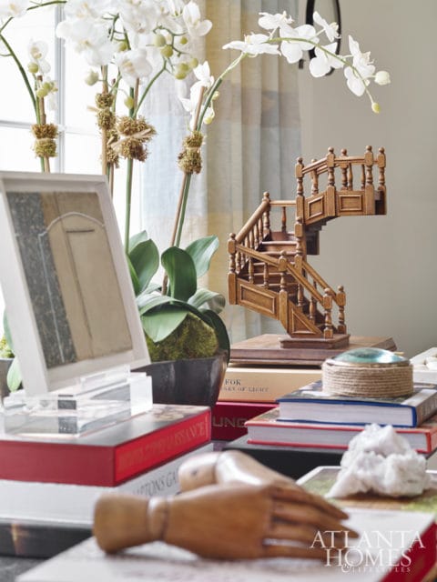 Close-up of a wooden model staircase on a stack of books, with white orchids and decorative objects on a table.