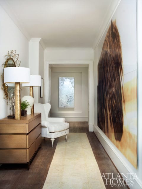 Hallway with a wooden dresser, white armchair, and large abstract artwork of a horse's mane.