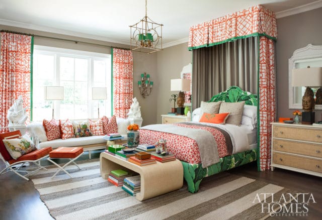 Bedroom with a green palm leaf headboard, orange and white patterned bedding, orange and white patterned curtains, and a white sofa with patterned pillows.