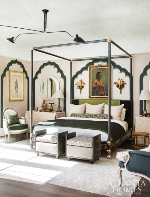 Bedroom with a dark metal four-poster bed, green headboard, and patterned pillows. Walls feature arched niches with green trim and artwork.