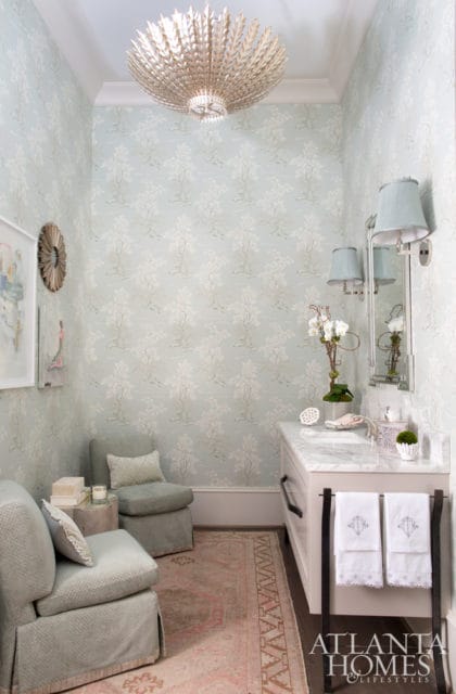 Powder room with light blue toile wallpaper, marble vanity, and two upholstered chairs. A large ornate chandelier hangs from the ceiling.