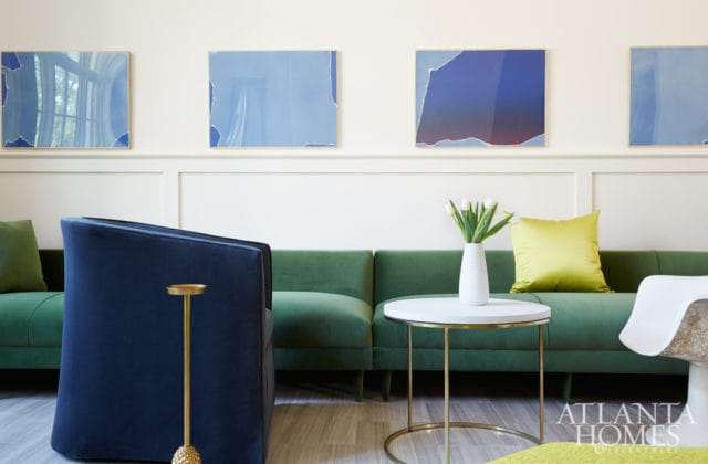 Living room with a navy blue velvet armchair, a green velvet sofa, abstract blue wall art, and a white round coffee table with tulips.