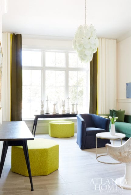 Living room with a large window, navy blue armchair, green sofa, lime green ottomans, and a white chandelier.