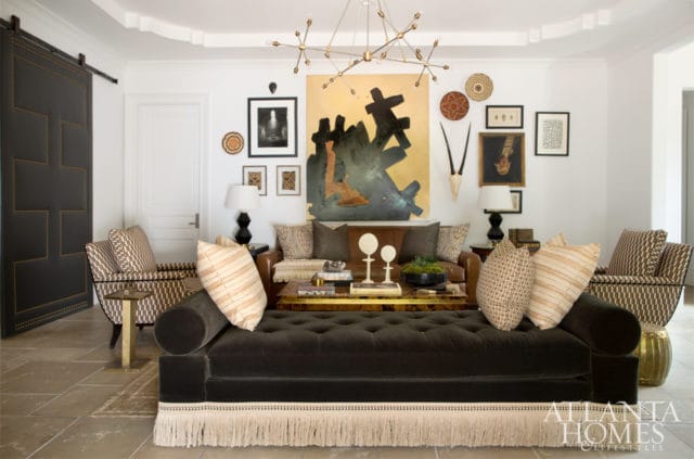 Living room with a dark tufted sofa with fringe, patterned armchairs, leather sofa, and abstract art above the fireplace.