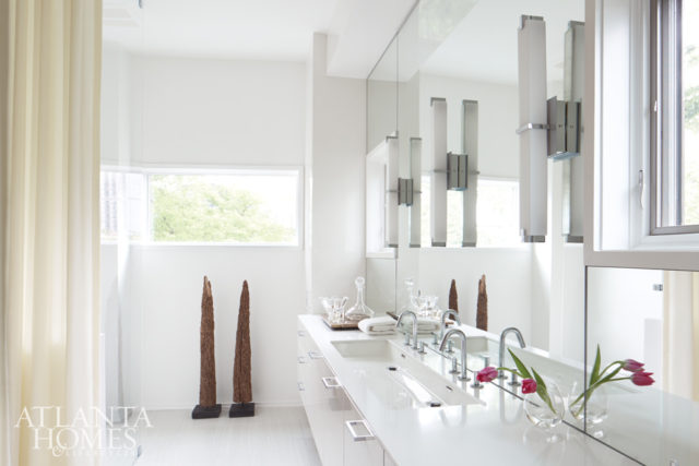 “The bath is actually quite small and irregularly shaped, so we kept everything white,” notes Musso. Sleek cabinetry by Design Galleria Kitchen and Bath Studio and geometric lighting from Tech Lighting reflect the home’s modern verve, while a pair of wooden sculptures add warmth.