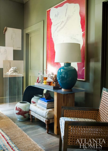 Green room with abstract art, teal lamp, cane chairs, and decorative vases.