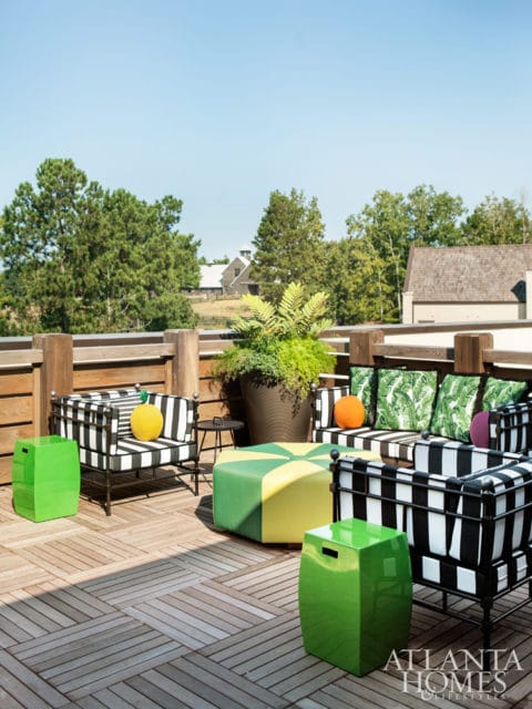 Outdoor seating area with black and white striped cushions, green and yellow ottoman, and bright green garden stools on a wooden deck.