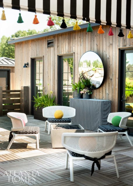 Outdoor patio with white wicker chairs, a concrete fire pit, and a striped cabinet against a wood-paneled building.