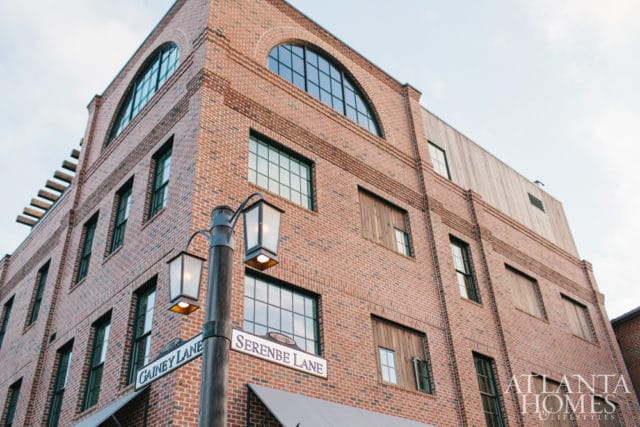 Brick building with arched windows and wooden accents, featuring street signs for Serenbe Lane and Gainey Lane, and an Atlanta Homes & Lifestyles logo.
