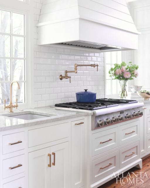 White kitchen with white subway tile backsplash, brass pot filler, stainless steel range, and marble countertops.