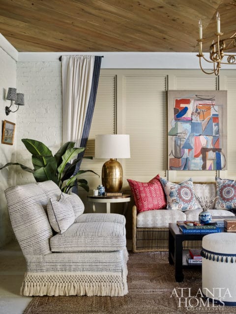 Living room with a textured armchair, a sofa with patterned pillows, a dark coffee table, and abstract art on the wall.