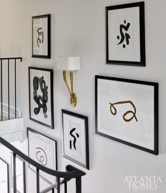 Hallway with a black metal banister, a gold sconce, and a gallery wall of framed abstract art in black and white.