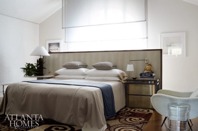 Bedroom with a king-size bed, neutral-toned bedding, striped accent pillows, a textured wall panel, and a modern armchair.