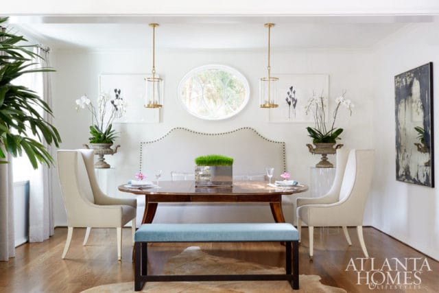 Dining room with oval wood table, upholstered chairs, and a light blue bench. A large upholstered headboard is behind the table, with two gold pendant lights overhead.
