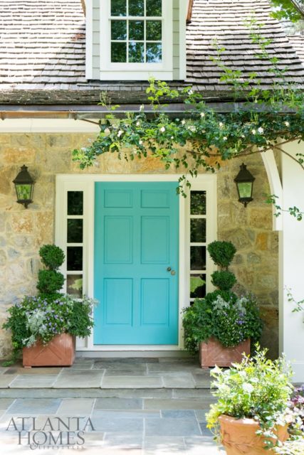 A bright turquoise front door is framed by intricate plantings.