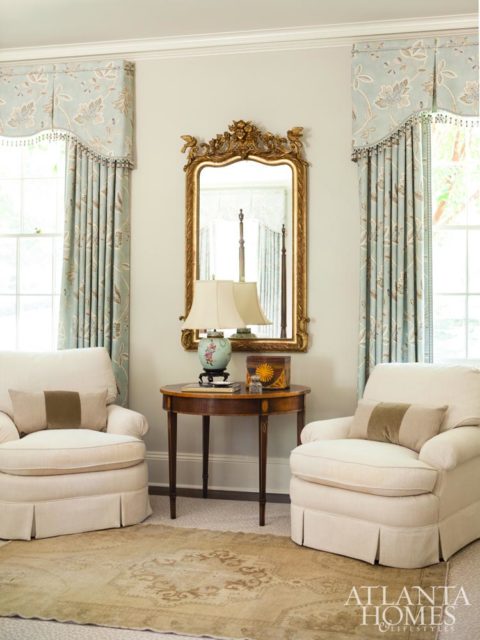 A guest retreat, dressed in a soft-blue, includes a sitting area with skirted chairs and a large antique gold mirror from New Orleans. Rug by Moattar.