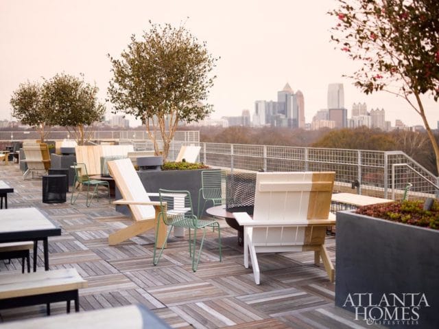 Rooftop patio with wooden deck, modern chairs, planters, and a city skyline in the background.