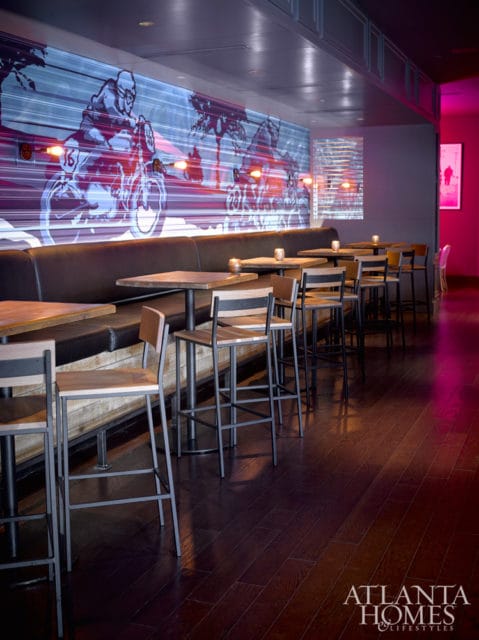 Bar area with dark wood floors, leather banquette seating, and tables with metal-frame stools. A large mural of motorcyclists and palm trees covers the back wall.
