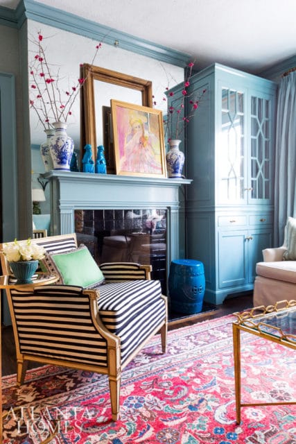 Living room with a light blue fireplace, a striped armchair, a blue cabinet, and a patterned rug.