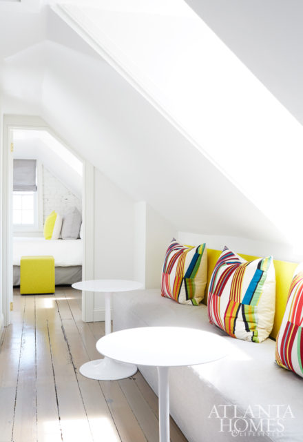 On the home’s fourth floor, a hallway leads to a small bedroom featuring twin beds—ideal for accommodating guests. The designer used a durable textile from BuzziSpace for the modular pouf, employing it once more as the backdrop for the upholstered hall bench.