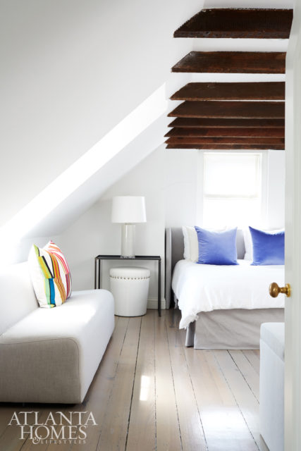 One of the home’s plush guest rooms features eye-catching original ceiling beams in a rich wood finish. “They had old carvings and dates on them. There was no way I was painting those,” Kay says. “They’re beautiful, and they make the house cozy.” The periwinkle velvet toss pillows and additional accent pieces are through South of Market.