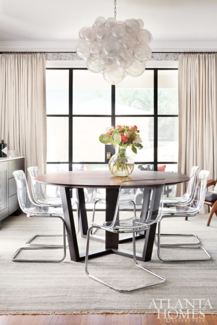 The dining room is a captivating space featuring a Muriel bubble chandelier from Oly, custom furniture, and the homeowner’s existing acrylic and chrome chairs.