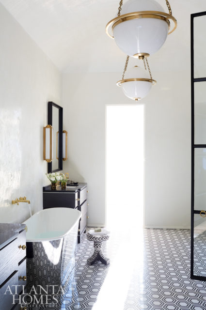 A barrel-vaulted ceiling creates a sense of openness in the master bathroom, where custom tile from SOURCE adds interest. Brass light fixtures give a nod to classic style, while custom cabinets stand out against white walls.