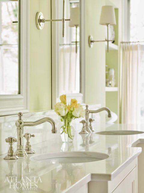 Double vanity bathroom with white marble countertop, polished nickel faucets, and a vase of yellow and white roses. Pale green walls and white trim are visible.