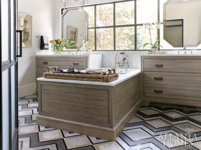 Bathroom with a freestanding tub, dual wood vanities with marble countertops, and a large window overlooking trees.