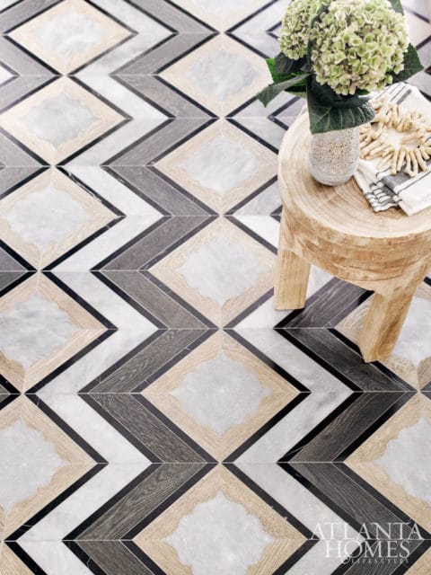 Geometric floor tile pattern with marble, wood, and black accents, featuring a wooden stool with a vase of flowers and a folded towel.