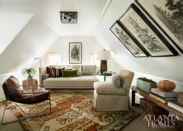 Attic living room with sloped white walls, a neutral daybed with colorful pillows, a leather armchair, and a patterned rug.