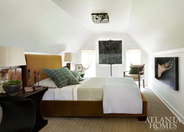 Attic bedroom with a mustard yellow upholstered bed, green plaid pillows, white quilted throw, and abstract art on the walls.