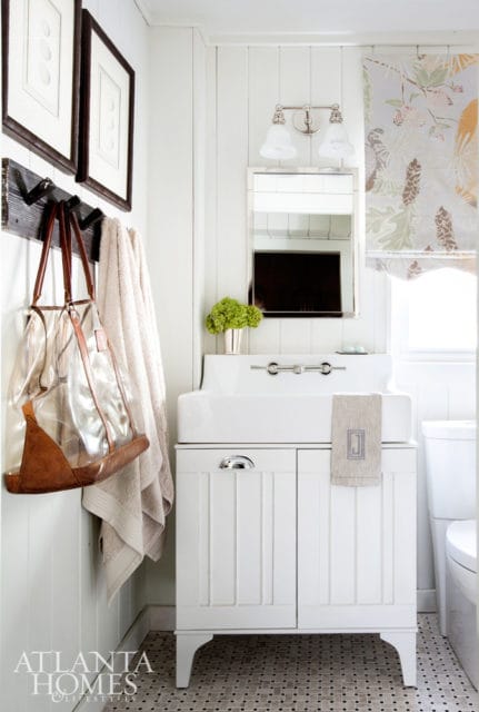 White bathroom vanity with a white sink, chrome faucet, and a mirrored cabinet below. A floral roman shade hangs above the sink.