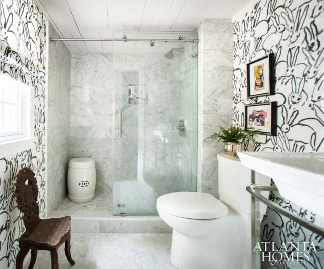 Bathroom with marble tile shower, white toilet, and black and white bunny wallpaper. A vintage wooden chair sits to the left.
