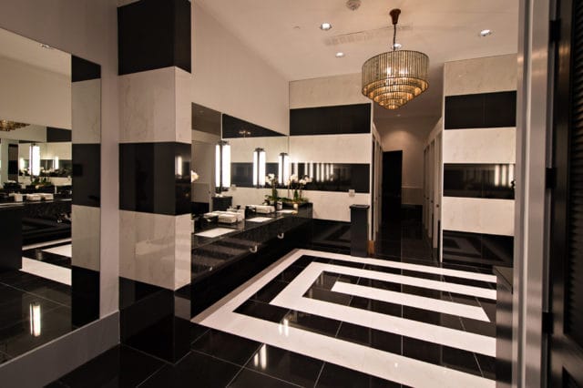 Guest bathroom with black and white marble tile, black granite countertops, a tiered chandelier, and a geometric floor pattern.