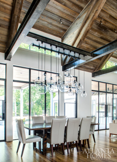 Steel-trimmed windows allow natural light to pour into the dining room, which looks out to the oasis-style pool, designed by J. Brownlee Design in Nashville. A custom industrial light fixture, designed and assembled by Patrick, holds court over the sleek mahogany table.