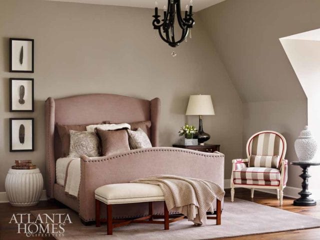 Bedroom with a pink upholstered wingback bed, striped accent chair, and framed feather art on a taupe wall.